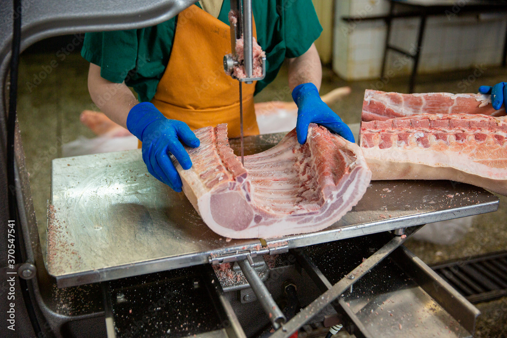 Slaughterhouse worker cuts pieces of pork into portions. The concept of sausage and delicatessen production.