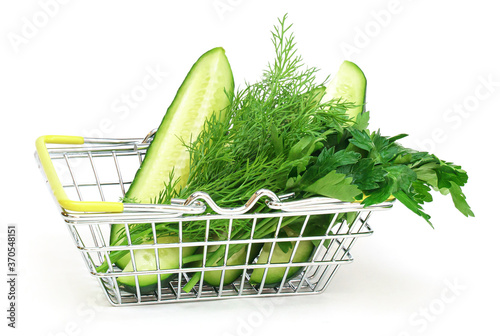 a small shopping basket with herbs, cucumber, tomato, parsley next to a fresh potted green salad on a white background. Healthy food, vegetarian food, vegetables, shopping at the supermarket.