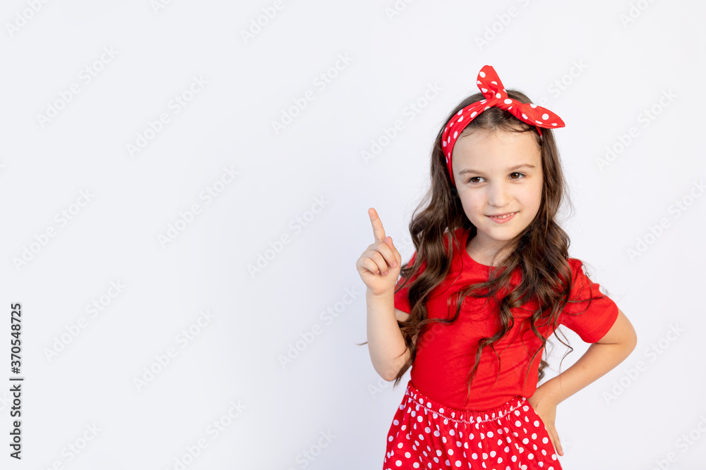 A cute little girl in a red outfit on a white isolated background shows a thumbs up. Space for text.the concept of the celebration and sales A cute little girl in a red outfit on a white isolated background shows a thumbs up. Space for text.the concept of the celebration and sales