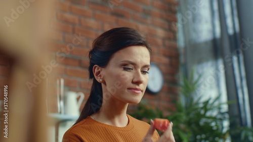 Woman tasting tomato in kitchen. Young girl eating piece of tomato at home