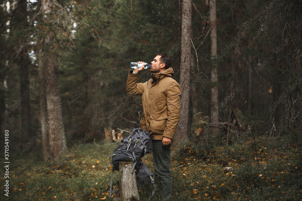Hiker with backpack drinking water in deep forest.