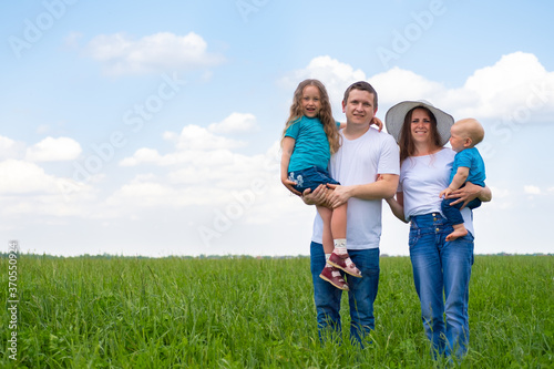 Portrait family dad, mom and two children boy and girl at summer against grass and blue sky. Happy caucasian parents with daughter and young son. Copyspace.