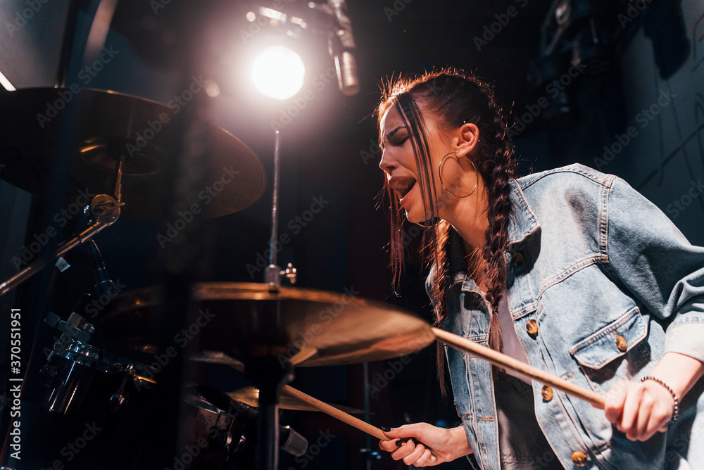 Fototapeta premium Plays drums. Young beautiful female performer rehearsing in a recording studio