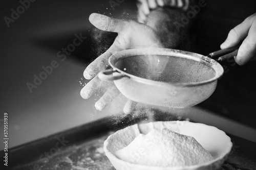 Foto A black-and-white image of a skilled chef using his hand to sift flour through a sieve into a bowl