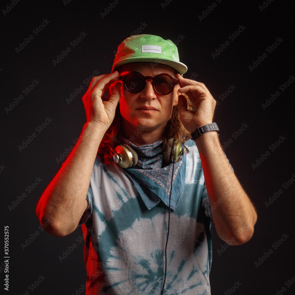 Studio portrait of a young man with long hairs in a green cap and headphones. Black background. Musician DJ Studio portrait of a young man with long hairs in a green cap and headphones. Black background. Musician DJ