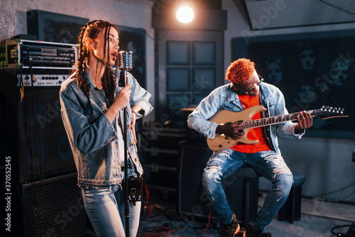 Guy plays guitar, girl sings. African american man with white girl rehearsing in the studio together