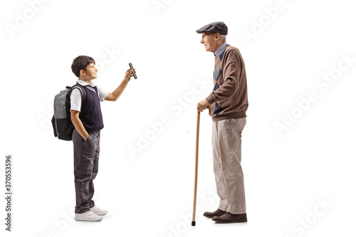 Schoolboy in a uniform standing and showing a smartphone to his grandfather