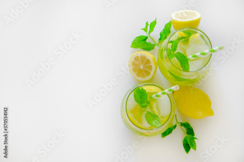 Two glasses of refreshing non alcoholic mojito drink with lemon slices, mint leaves and ice. Studio shot of iced lemonade isolated on white background, close up, copy space, top view.