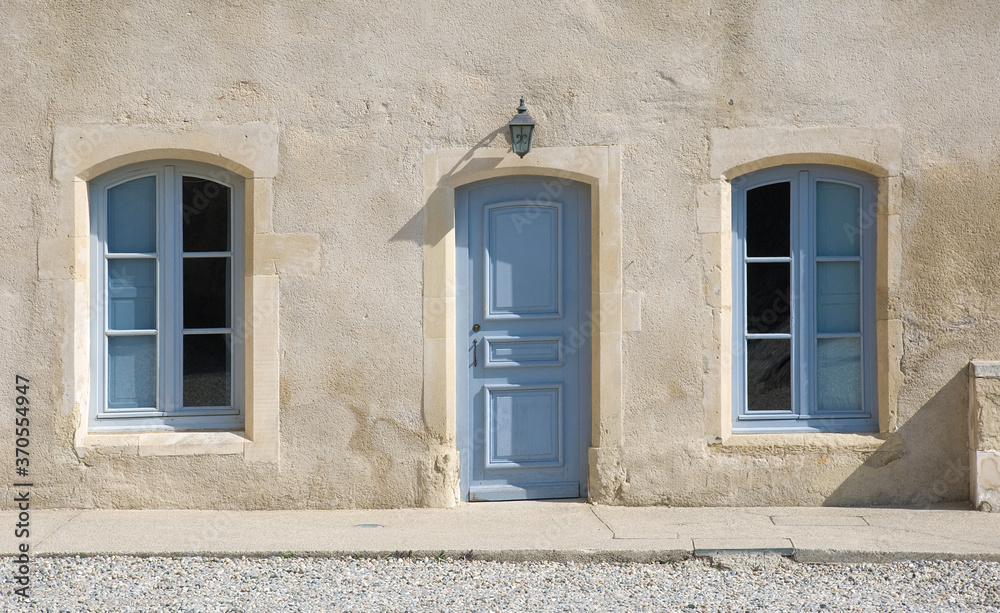 Pittoreske naturfarbene, helle Wand mit hellblauer Tür und Fenstern