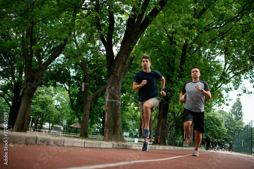 Young men training on a race track. Two young friends running on the athletics track.