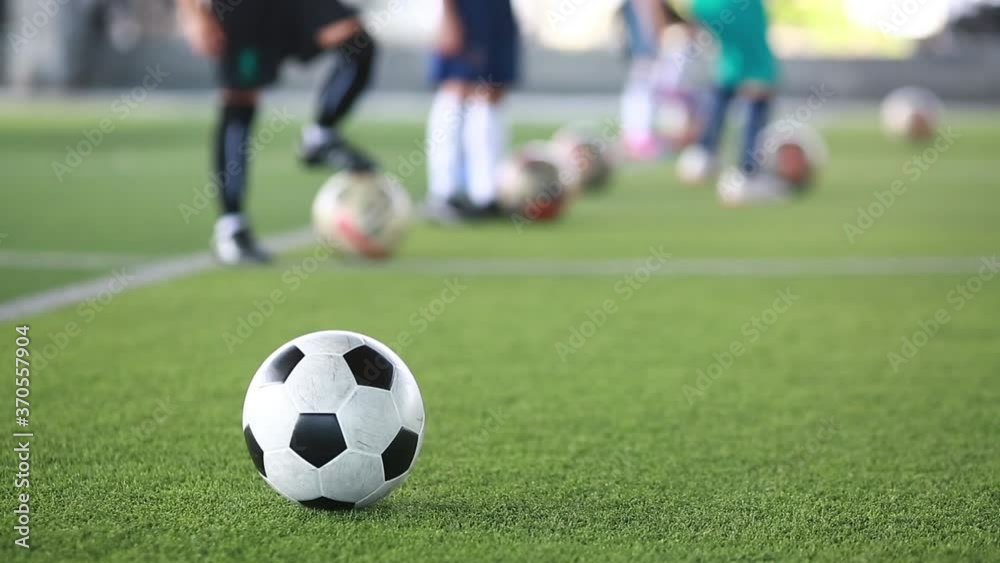 Soccer ball moving on green artificial turf with blurry kid soccer team training in soccer academy. Soccer ball moving on green artificial turf with blurry kid soccer team training in soccer academy.