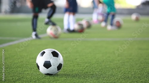 Soccer ball moving on green artificial turf with blurry kid soccer team training in soccer academy.