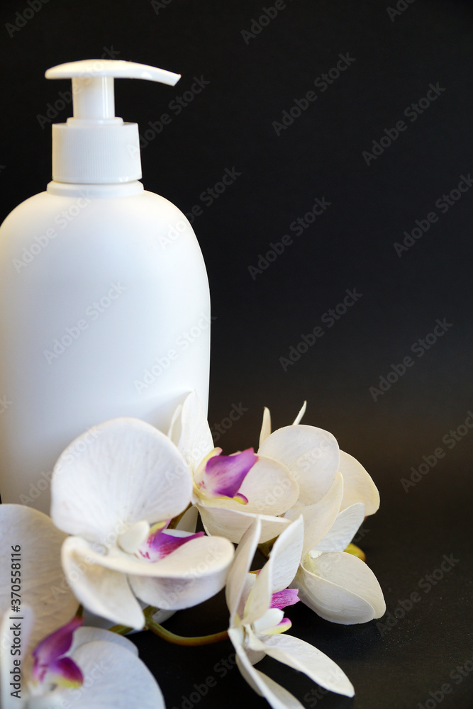 white cosmetic bottle and white orchid flower on a black background close-up