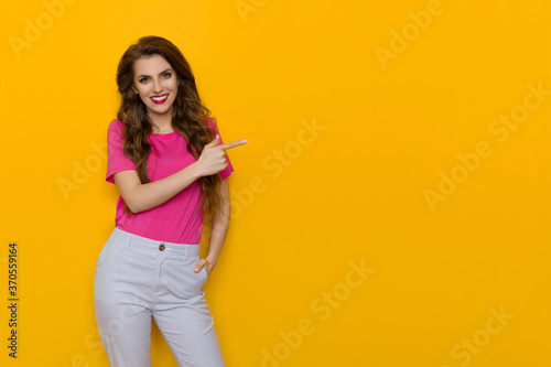 Smiling Young Woman In Pink T-Shirt Is Pointing At The Side