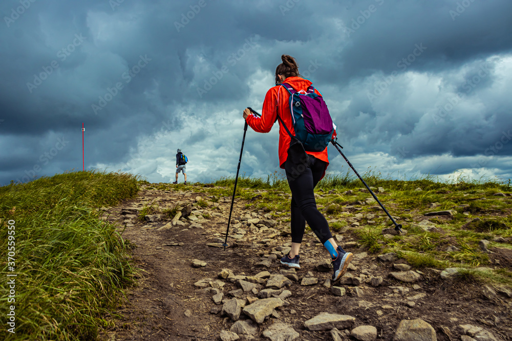 Hiker in the mountains. Storm clouds over the mountains. Girl hiking with a sticks.