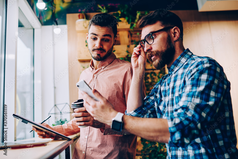Emotional hipster guy looking at smartphone notification and shocked with receiving receipt bill, stressed young man reading bad news getting message on cellular with his friend feeling disappointed Emotional hipster guy looking at smartphone notification and shocked with receiving receipt bill, stressed young man reading bad news getting message on cellular with his friend feeling disappointed