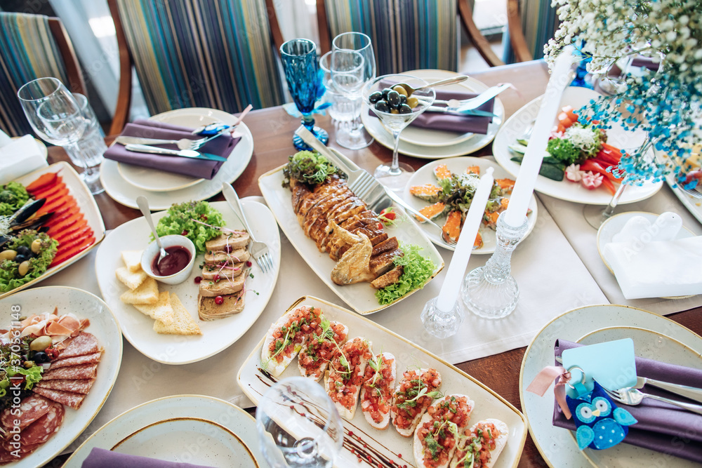 Beautiful wedding table set in a restaurant with food on plates, decor and candlesticks on a white tablecloth Beautiful wedding table set in a restaurant with food on plates, decor and candlesticks on a white tablecloth