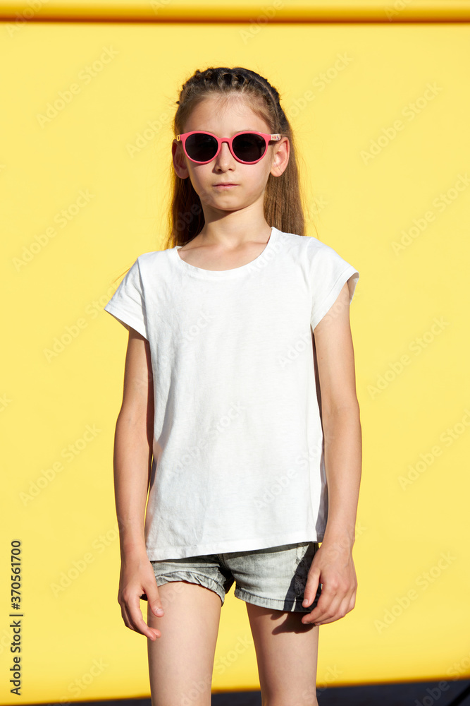Fototapeta premium Kid girl wearing white t-shirt with space for your logo or design over yellow backdrop