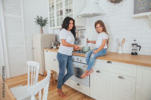 Happy loving family preparing dinner together. Smiling Mom and child daughter girl cooking and having fun in the kitchen. Homemade healthy food. Little helper in the white Scandinavian-style interior. © Алина Троева