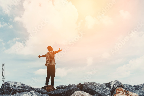Man raise hand up at top of rock on blue sky and white cloud abstract background. Freedom feel good and travel adventure vacation concept.