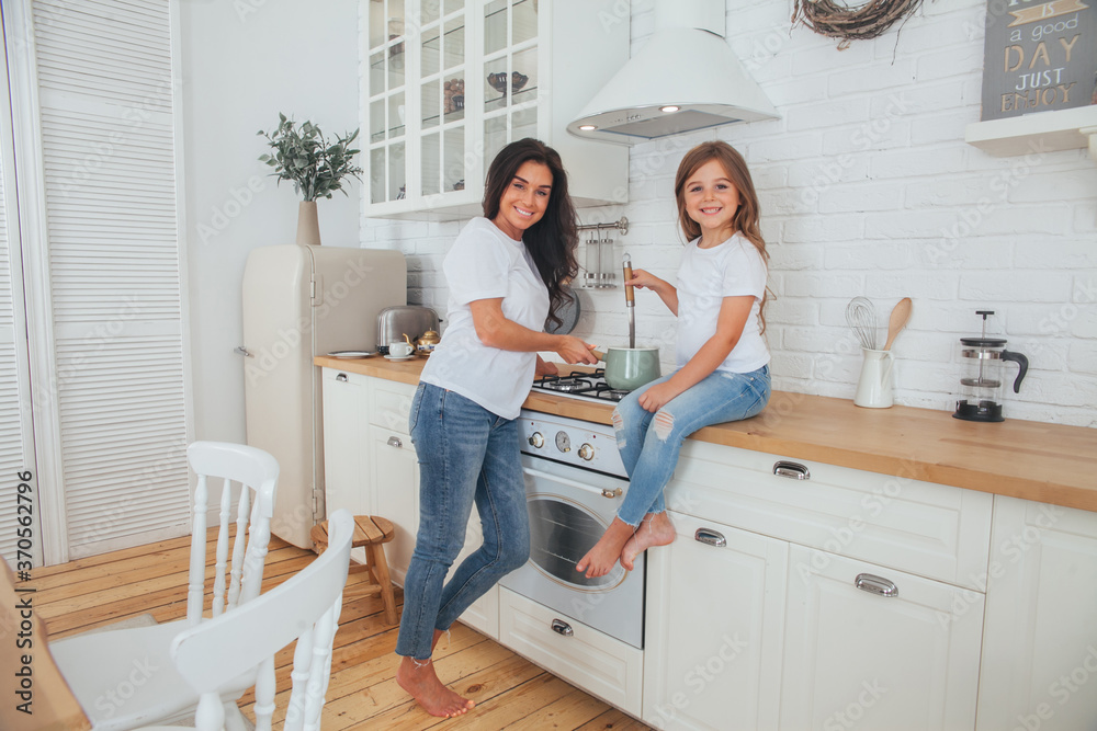 Happy loving family preparing dinner together. Smiling Mom and child daughter girl cooking and having fun in the kitchen. Homemade healthy food. Little helper in the white Scandinavian-style interior. Happy loving family preparing dinner together. Smiling Mom and child daughter girl cooking and having fun in the kitchen. Homemade healthy food. Little helper in the white Scandinavian-style interior.
