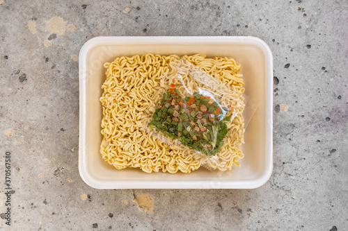 Top view open plastic box with raw instant noodles with seasoning, ready for cooking.  Close up on a gray stone background