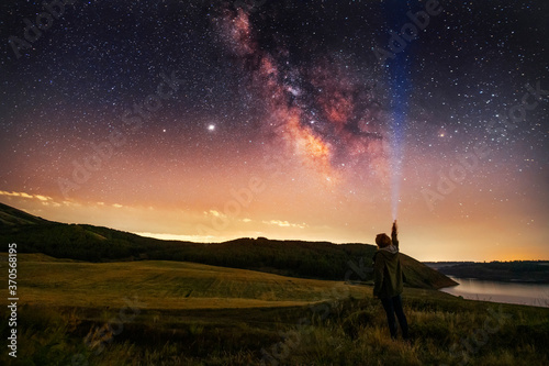 Beautiful starry sky with bright milky way galaxy. Night landscape . Person silhouette with flashlight illuminate starry sky.