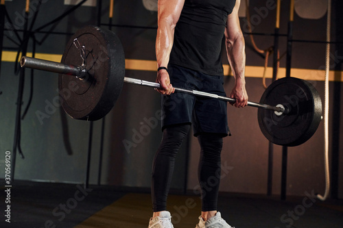Strong man in sportive clothes lifting barbell in the gym