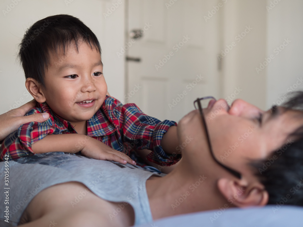 Asian little cute child boy playing with father in bedroom with happy smiling face. Son and dad have relaxing time together at home with love. Kid laughing with happiness in summer holiday. Asian little cute child boy playing with father in bedroom with happy smiling face. Son and dad have relaxing time together at home with love. Kid laughing with happiness in summer holiday.