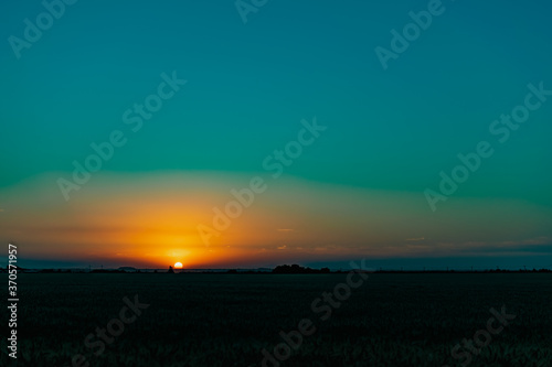 Beautiful evening sunset over a field of Golden ears of wheat and barley. Yellow is the rich color of the Sunny sky and wide spacious meadows with crops