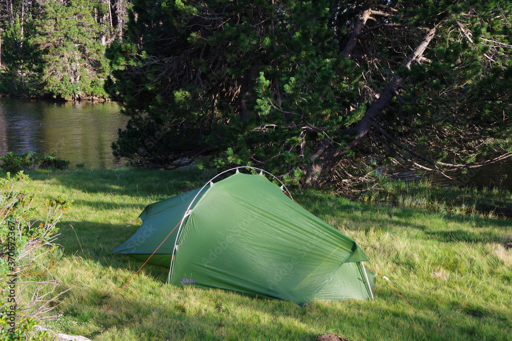Tente verte de bivouac et de camping sur la pelouse en forêt au bord de l'eau du lac de montagne