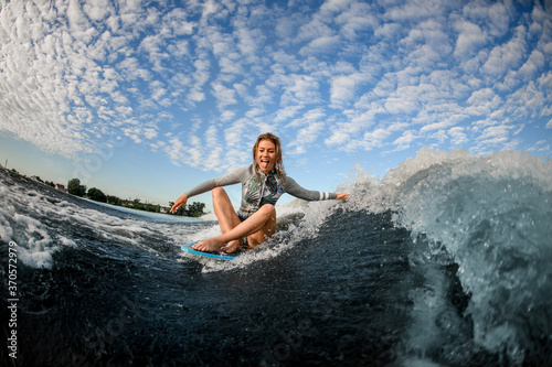 cheerful woman sits on wakesurf board and rides the wave and touches the waves with one hand