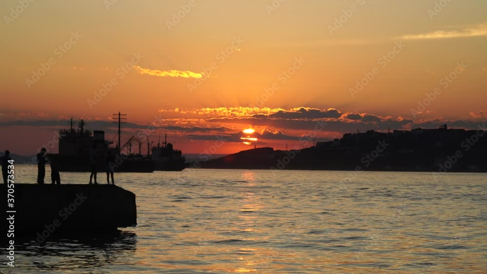 Seascape with silhouettes of fishermen and a ship at sunset. Vladivostok, Russia Seascape with silhouettes of fishermen and a ship at sunset. Vladivostok, Russia