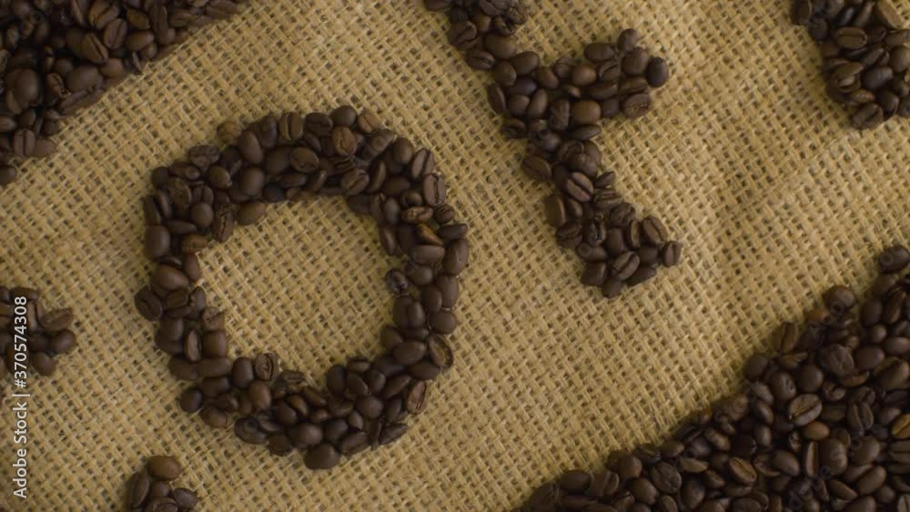 Close up Coffee word lined with roasted coffee beans on burlap. Raw fresh food concept. Hand placed down a a cup of coffee. Camera slowly moving on slider, dolly shot, top view. Texture, background Close up Coffee word lined with roasted coffee beans on burlap. Raw fresh food concept. Hand placed down a a cup of coffee. Camera slowly moving on slider, dolly shot, top view. Texture, background