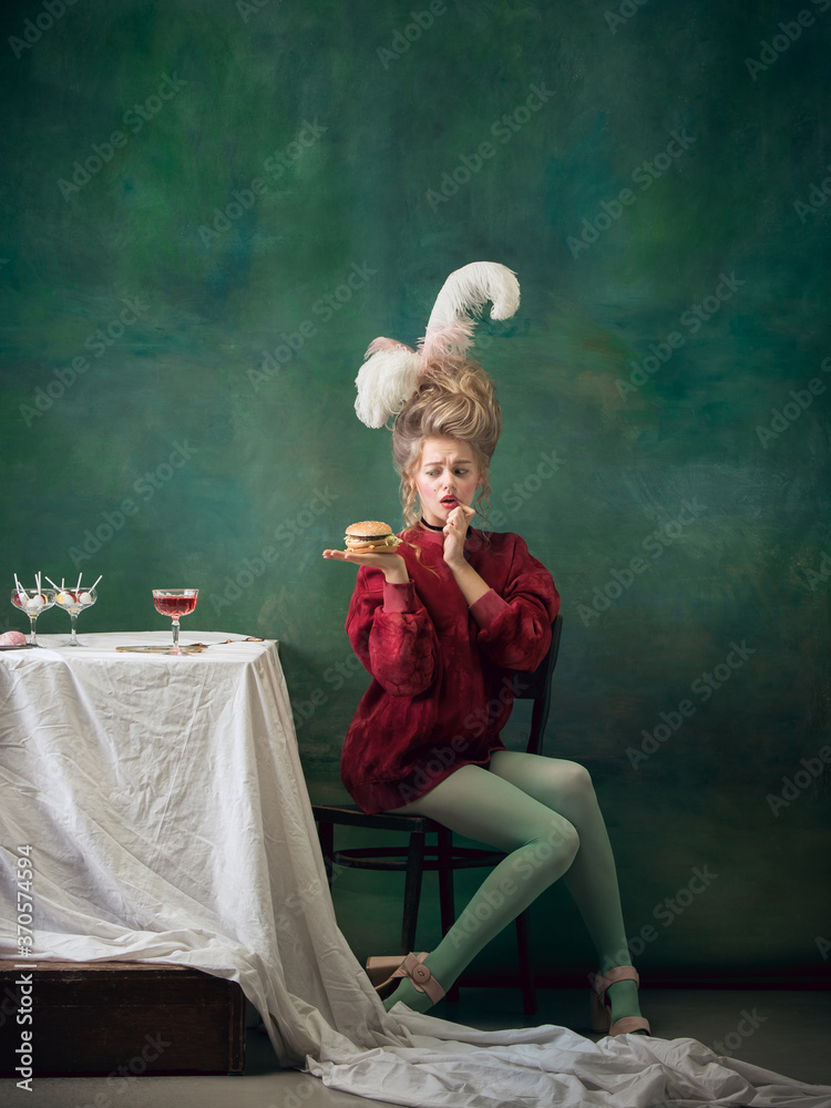 Such a welcome burger. Young woman as Marie Antoinette on dark green background. Retro style, comparison of eras concept. Beautiful female model like classic historical character, old-fashioned.