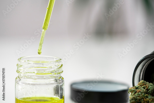 Close up of a pipette dropping medical cannabis oil into a glass with marijuana buds around 