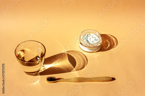 Bamboo toothbrush, glass of water and toothpaste powder on a peach-colored pastel background. Biodegradable pesonal care and plastic free zero waste concept. Top view. Shadows.