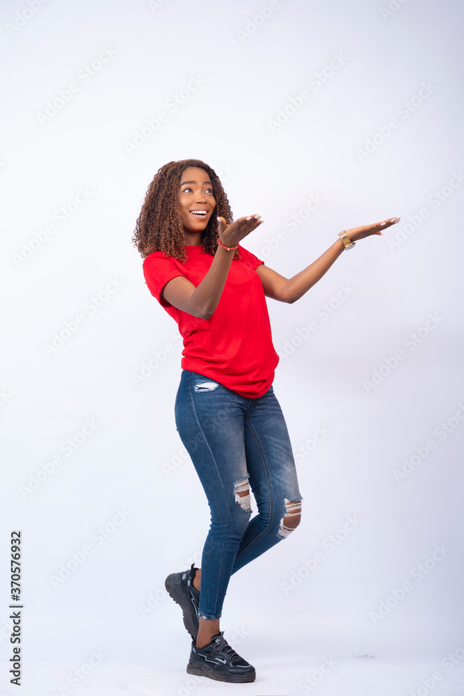 confident young black woman posing in front of white background, feeling delighted gesturing to her side