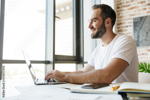 Image of cheerful man working with laptop while sitting at table