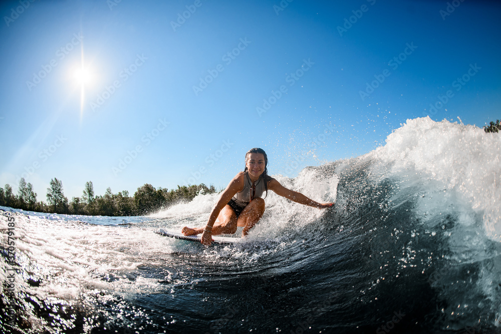 smiling woman sits on wakesurf board and rides the wave