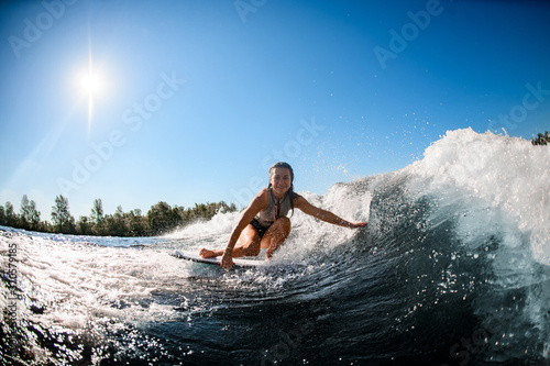 smiling woman sits on wakesurf board and rides the wave