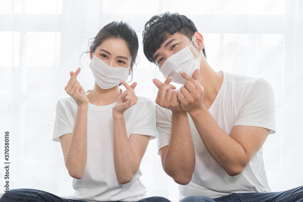 Asian couple wearing protective face mask and making shape of Heart by their Hands at home.