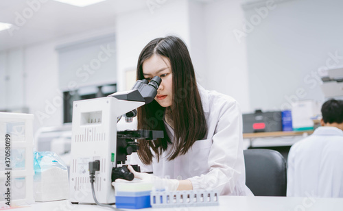 young female medical scientist looking at microscope in laboratory.