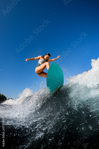 view of sporty woman in gray swimsuit who jumps with bright surf board.