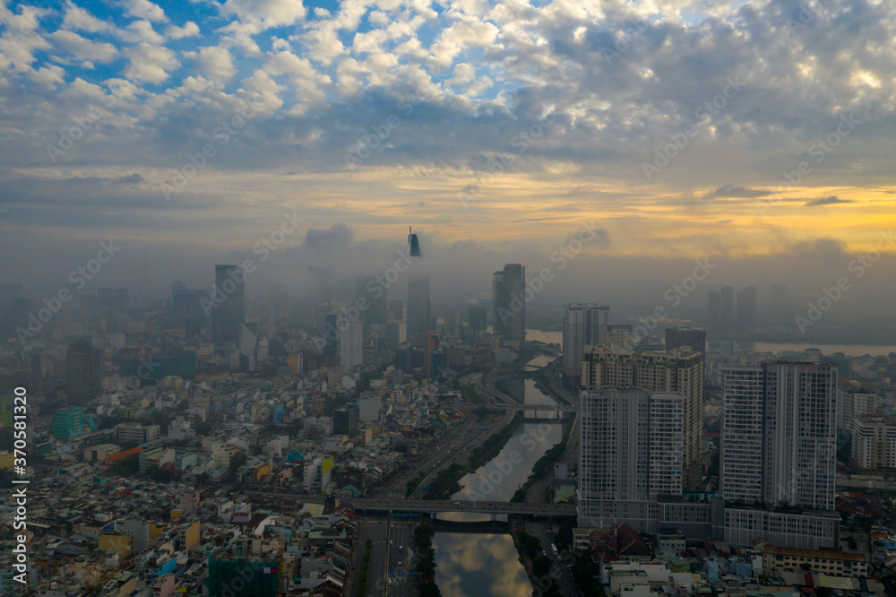 Beautiful aerial photo of colorful sunrise and morning fog in Ho Chi Minh City featuring the canal, bridges Saigon River and high rise buildings obscured by low cloud