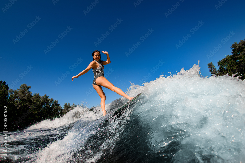 young wet woman confidently stands on the wakesurf board and rides the wave