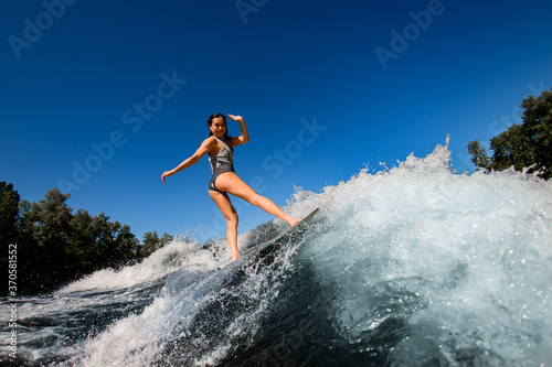 young wet woman confidently stands on the wakesurf board and rides the wave