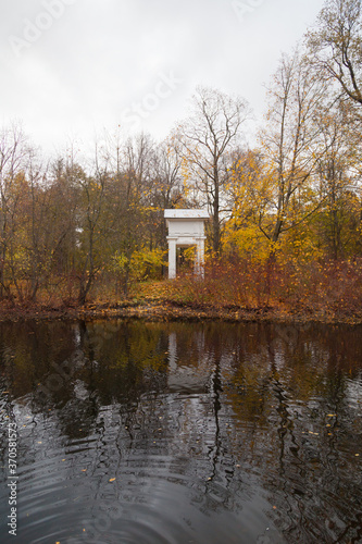 White arch among autumn trees reflected in a pond