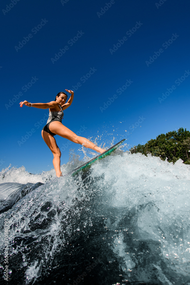 young wet woman energetically rides the wave on wakesurf board