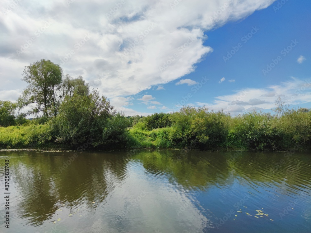 Fototapeta premium green river bank against the background of a beautiful blue sky with clouds